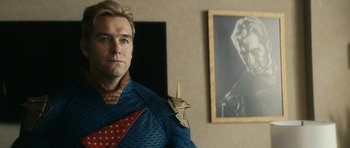 Movie still from “The Boys” (2019), created by Eric Kripke – A man in a blue and red suit standing in front of a picture; Medium shot, Over the shoulder angle