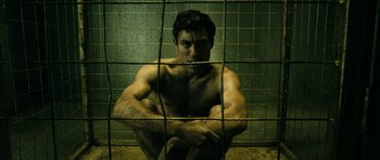 Movie still from “The Boys” (2019), created by Eric Kripke – A man sitting in a cage with his arms crossed; Medium shot, High angle