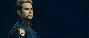 Movie still from “The Boys” (2019), created by Eric Kripke – A man with a headset is standing in front of a wall; Close Up shot, Over the shoulder angle