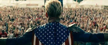 Movie still from “The Boys” (2019), created by Eric Kripke – A person wearing an american flag shirt in front of an audience; Medium shot, Overhead angle