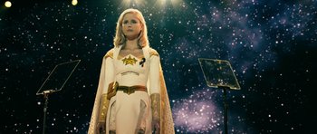 Movie still from “The Boys” (2019), created by Eric Kripke – A woman dressed in a white and gold costume stands in front of a microphone; Medium shot, Low angle