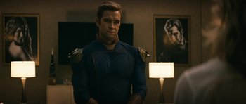 Movie still from “The Boys” (2019), created by Eric Kripke – A man in a blue and black uniform standing in front of a lamp; Medium shot, Over the shoulder angle