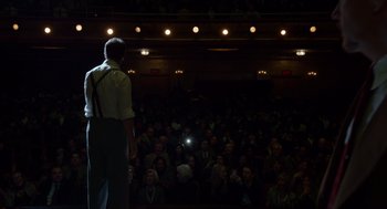 Movie still from “Birdman or (The Unexpected Virtue of Ignorance)” (2014), directed by Alejandro G. Iñárritu – A man standing in front of an audience with a cell phone; Wide shot, Low angle
