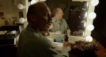 Movie still from “Birdman or (The Unexpected Virtue of Ignorance)” (2014), directed by Alejandro G. Iñárritu – A man holding a gun in front of a bathroom mirror; Medium shot, Over the shoulder angle