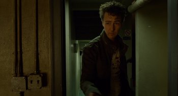 Movie still from “Birdman or (The Unexpected Virtue of Ignorance)” (2014), directed by Alejandro G. Iñárritu – A young man in a brown jacket standing next to a door; Medium shot, Over the shoulder angle
