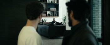 Movie still from “The Boys” (2019), created by Eric Kripke – A man sitting on top of a black couch in a living room; Wide shot, Over the shoulder angle