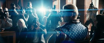 Movie still from “The Boys” (2019), created by Eric Kripke – A group of people taking pictures of a woman wearing a flag shirt; Medium shot, Low angle