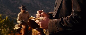 Movie still from “3:10 to Yuma” (2007), directed by James Mangold – A person writing in a notebook on a hill; Close Up shot, Over the shoulder angle