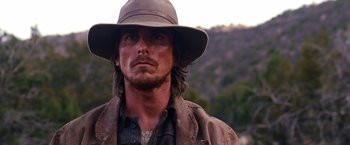 Movie still from “3:10 to Yuma” (2007), directed by James Mangold – A person wearing a hat with trees in the background; Close Up shot, Over the shoulder angle