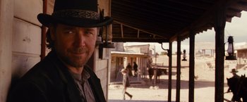 Movie still from “3:10 to Yuma” (2007), directed by James Mangold – A man wearing a top hat standing in front of a building; Close Up shot, Over the shoulder angle