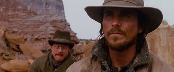 Movie still from “3:10 to Yuma” (2007), directed by James Mangold – A man with a hat and a beard standing next to another man with a hat; Close Up shot, Over the shoulder angle