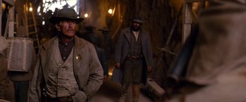 Movie still from “3:10 to Yuma” (2007), directed by James Mangold – A man in a hat is standing next to another man in a coat; Medium shot, Over the shoulder angle