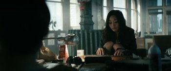 Movie still from “The Boys” (2019), created by Eric Kripke – A woman sitting at a table using a laptop computer; Medium shot, High angle