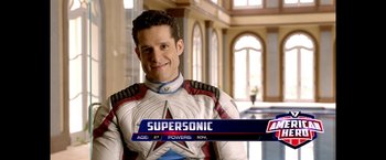 Movie still from “The Boys” (2019), created by Eric Kripke – A man in a white and red suit smiling for the camera; Medium shot, Over the shoulder angle