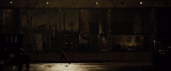 Movie still from “The Curious Case of Benjamin Button” (2008), directed by David Fincher – A person running on the street in front of a building at night; Extreme Wide shot, High angle