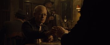 Movie still from “The Curious Case of Benjamin Button” (2008), directed by David Fincher – A man sitting at a table with another man holding his hand; Medium shot, Over the shoulder angle
