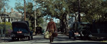 Movie still from “The Curious Case of Benjamin Button” (2008), directed by David Fincher – A man walking down the street carrying bags of luggage; Wide shot, Over the shoulder angle