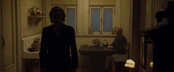 Movie still from “The Curious Case of Benjamin Button” (2008), directed by David Fincher – A woman standing in front of a table with a man sitting at the table; Wide shot, Over the shoulder angle