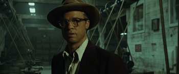 Movie still from “The Curious Case of Benjamin Button” (2008), directed by David Fincher – A man wearing a hat and glasses standing in a dark room; Close Up shot, Low angle