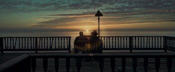 Two people sitting on a bench watching the sun go down over the ocean