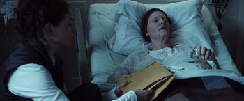 Movie still from “The Curious Case of Benjamin Button” (2008), directed by David Fincher – An older woman laying in a hospital bed holding an envelope; Close Up shot, Overhead angle