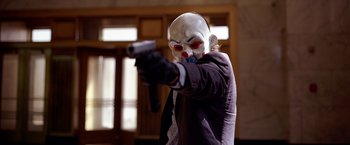 Movie still from “The Dark Knight” (2008), directed by Christopher Nolan – A person in a clown mask holding a gun; Medium shot, Low angle