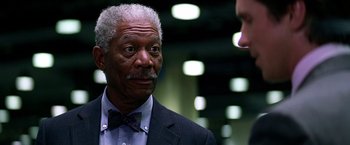 Movie still from “The Dark Knight” (2008), directed by Christopher Nolan – An older man wearing a suit and a bow tie; Close Up shot, Over the shoulder angle