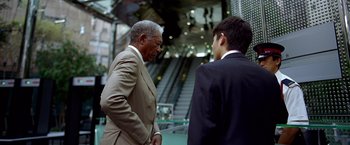 Movie still from “The Dark Knight” (2008), directed by Christopher Nolan – Two men in suits standing next to each other in front of an escalator; Medium shot, Low angle