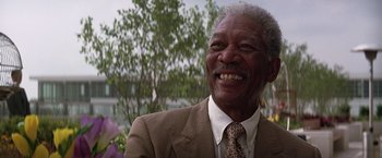 Movie still from “The Dark Knight” (2008), directed by Christopher Nolan – An older man wearing a suit and tie smiling for the camera; Close Up shot, Low angle