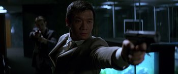 Movie still from “The Dark Knight” (2008), directed by Christopher Nolan – A man wearing a suit and tie holding a gun; Close Up shot, Low angle