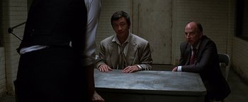 Movie still from “The Dark Knight” (2008), directed by Christopher Nolan – A man sitting at a table in front of another man; Medium shot, Over the shoulder angle