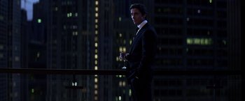 Movie still from “The Dark Knight” (2008), directed by Christopher Nolan – A man in a black suit standing in front of a window; Medium shot, Low angle