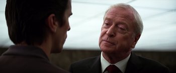 Movie still from “The Dark Knight” (2008), directed by Christopher Nolan – An older man wearing a suit and tie talking to a younger man; Close Up shot, Over the shoulder angle