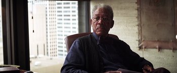 Movie still from “The Dark Knight” (2008), directed by Christopher Nolan – An older man sitting in a chair in front of a window; Close Up shot, High angle