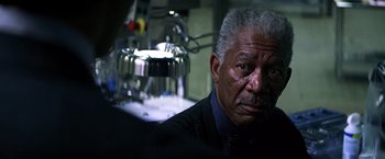 Movie still from “The Dark Knight” (2008), directed by Christopher Nolan – An older man in a suit and tie looking at the camera; Close Up shot, Over the shoulder angle