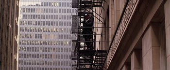 Movie still from “The Dark Knight” (2008), directed by Christopher Nolan – A man standing on top of a fire escape on the side of a building; Wide shot, Low angle