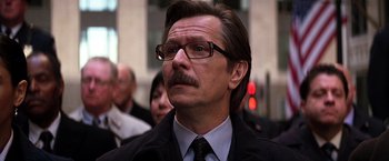 Movie still from “The Dark Knight” (2008), directed by Christopher Nolan – A person wearing glasses and a tie; Close Up shot, Low angle
