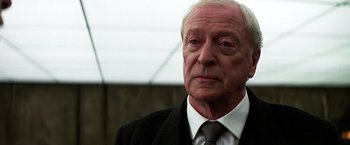 Movie still from “The Dark Knight” (2008), directed by Christopher Nolan – An older man wearing a suit and tie; Close Up shot, Low angle