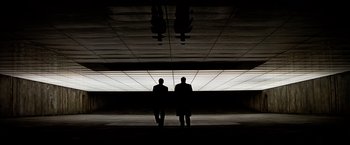 Movie still from “The Dark Knight” (2008), directed by Christopher Nolan – Two men in suits are standing under a ceiling; Extreme Wide shot, Low angle