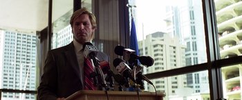 Movie still from “The Dark Knight” (2008), directed by Christopher Nolan – A man standing at a podium in front of microphones; Medium shot, Low angle