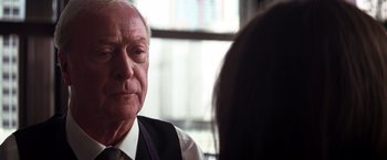 Movie still from “The Dark Knight” (2008), directed by Christopher Nolan – An older man wearing a vest and a tie; Close Up shot, Over the shoulder angle