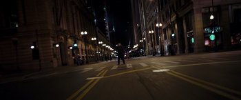 Movie still from “The Dark Knight” (2008), directed by Christopher Nolan – A person riding a skate board on a city street at night; Extreme Wide shot, High angle