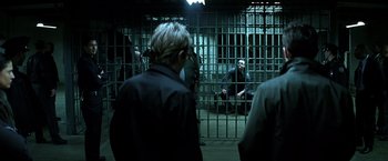 Movie still from “The Dark Knight” (2008), directed by Christopher Nolan – A group of people sitting in front of a jail cell; Wide shot, Over the shoulder angle