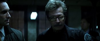 Movie still from “The Dark Knight” (2008), directed by Christopher Nolan – A person wearing glasses and a black shirt; Close Up shot, Low angle