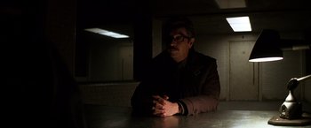 Movie still from “The Dark Knight” (2008), directed by Christopher Nolan – A man sitting at a table in a dark room; Medium shot, Over the shoulder angle