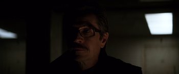 Movie still from “The Dark Knight” (2008), directed by Christopher Nolan – A person wearing glasses and a black shirt; Close Up shot, Low angle