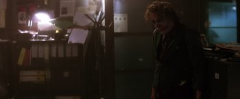 Movie still from “The Dark Knight” (2008), directed by Christopher Nolan – A man in a dark room with a joker mask on; Medium shot, Over the shoulder angle