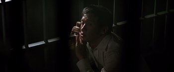 Movie still from “The Dark Knight” (2008), directed by Christopher Nolan – A man sitting in the dark talking on a cell phone; Close Up shot, Low angle