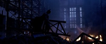 Movie still from “The Dark Knight” (2008), directed by Christopher Nolan – A man dressed as the dark knight walks through the rubble; Wide shot, Low angle