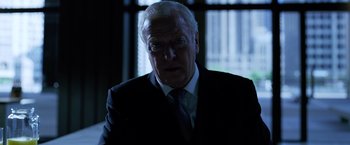 Movie still from “The Dark Knight” (2008), directed by Christopher Nolan – An older man wearing a suit and tie in front of a window; Close Up shot, Low angle